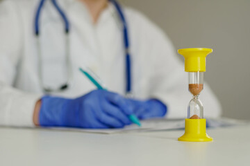 Hourglass with time running out and doctor in lab coat taking notes or prescription in journal.