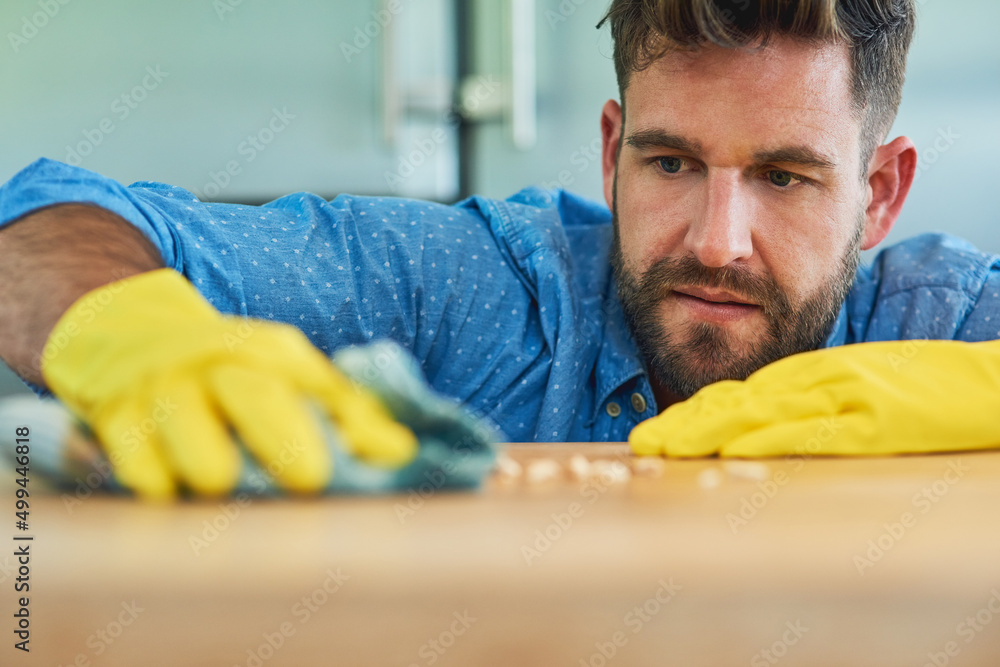 Poster powering through household chores like a champ. shot of a man wearing rubber gloves while wiping a t