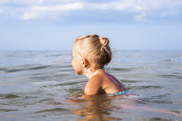 Fototapeta na wymiar Child blond girl with her back swimming in the sea.