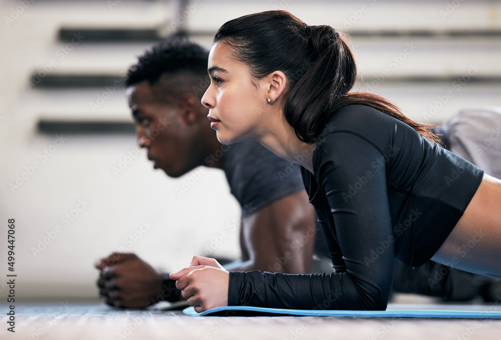 Wall mural Where strong bodies begin. Shot of a young man and woman doing plank exercises in a gym.