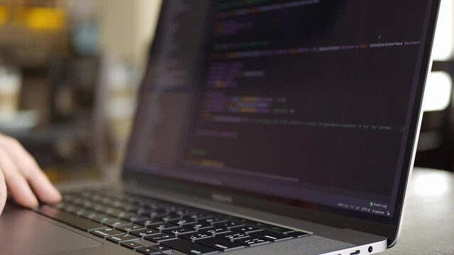 Male hands scrolling code on silver notebook screen. A caucasian young man works on a laptop in a cafe or coworking space