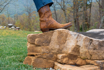 Lady with her foot on a rock wearing cowboy boots, in the mountains.