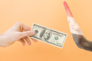 Say no dollar. The hand gesture of Iraq rejects dollars. One arm holds 100 dollars, and the other arm painted with the Iraqi flag doesn't want to take it. Isolated on yellow background. Wrong