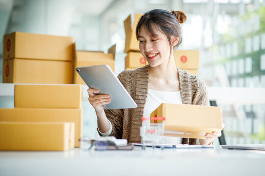 Startup small business entrepreneur SME or freelance Young Asian woman using a laptop computer with box, successful Asian woman working, online marketing packaging delivery, SME online business ideas.