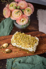 Pistazienkuchen auf Holzbrett mit Ranunkeln im Hintergrund