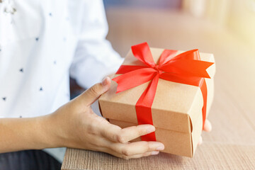 Female hands holding a gift wrapped with red ribbon