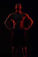 Strong and muscular man posing in the studio with colored lights