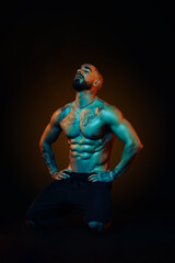 Strong and muscular man posing in the studio with colored lights