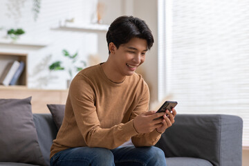 Obraz premium Asian man is smiling on the cellphone like he got a good news. The man seems so happy with the mobile phone screen. Technology make us have a convenience life and also make the world getting smaller.