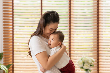 Asian mom holding her baby newborn in hand and kissing baby sweet and lovely.Good moment of Happy mother and infant baby looking together smile with love.Mother and baby newborn Concept