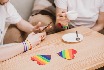 Lesbian couple drinking coffee in a cafe and serfing in smartphone close up. Hands holding rainbow hearts
