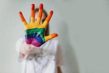Woman shows rainbow painted hand close her face in stop gesture. Equal rights. Stop discrimination