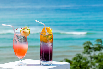 Two glasses of chilled non-alcoholic tasty tropical cocktails with slices of orange and lime in hot summer sunny day with ocean on background. Close-up of refreshment mocktails. Travel concept
