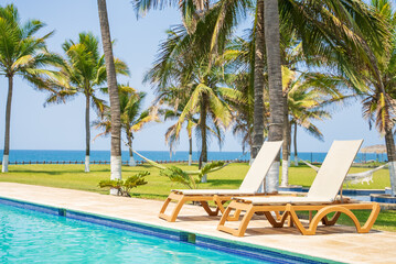 Fototapeta na wymiar pool in a tropical location with a beach. Poolside beds, hammocks, palm trees and the ocean can be seen