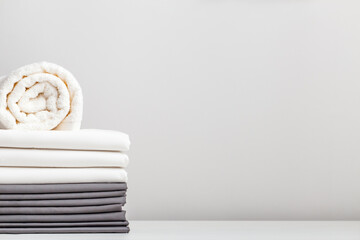 A stack of gray and white linens, sheets and a terry towel on the table.