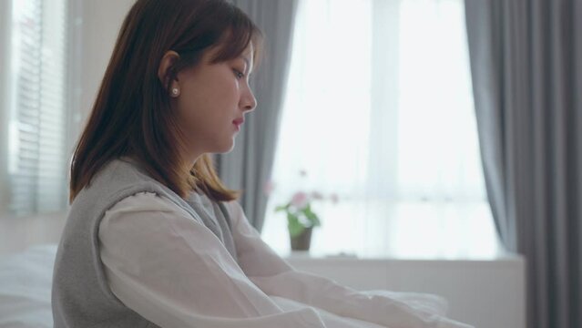 Anxiety young Asian woman depressed and stressed sitting with head in hands in the bedroom. Unhealthy mental ill female suffers from insomnia. Negative emotion concept.