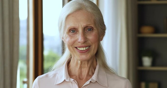 Head shot portrait long haired hoary senior female retiree stand indoors at living room look at camera with white toothy healthy smile. Happy aged lady advertizing dental care service for aged persons
