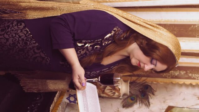A Jewish woman in a wig and a headscarf falling from her hair performs a siddur ritual with wine after Shabbat. vertical video