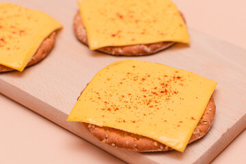 Crispy Cracker Sandwiches with Cheese and Paprika on Wooden Cutting Board and Beige Background