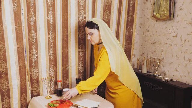 A Jewish woman in a wig and a head veil takes a beitz egg and a jug of salt water in her hand to fulfill the commandment. Overall plan