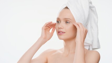 Young Caucasian woman with hair-drying towel on her head gently touches her face after bathroom on white background | Soft skin commercial concept