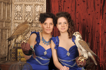 two women in blue dresses, mother and daughter, in a vintage interior with a falcon