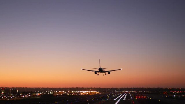 Airport runway lights at night, plane or airplane landing to airstrip, twilight dusk and sunset. Airliner jet arriving to aerodrome, San Diego airfield, California USA. Aircraft flying mid air in sky.
