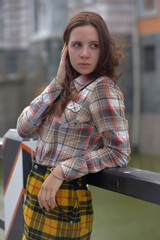 pretty brunette girl in a plaid blouse and skirt on a city street