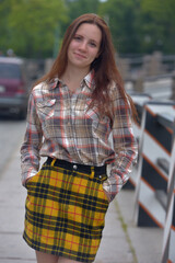 pretty brunette girl in a plaid blouse and skirt on a city street - 499462609
