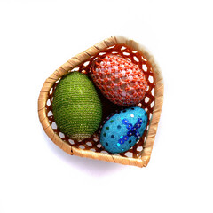 Handmade Easter eggs made of beads in a wicker basket in the shape of a heart. white background.