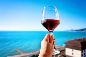 a woman's hand holds a glass of red wine from the hotel window against the background of the blue sea on a sunny day at the resort