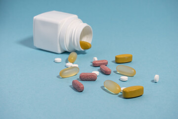 The colored pills and vitamins and white container on the blue background