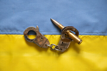 Handcuffs and a bullet lie on the yellow-blue flag of Ukraine, laws in Ukraine, democracy and war...