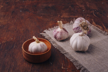 Garlic bulbs on sackcloth, in pot, wooden table. Spicy vegetable, piquant flavouring, organic food, healthy eating, cooking ingredient