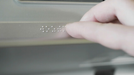 Close up of male hand touching Braille on a metal sign. HDR. Visually impaired or blind person...