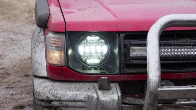 Front diode headlights of an old SUV. A very dirty car, painted red.