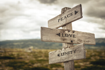 peace love unity text quote written in wooden signpost outdoors in nature. Moody theme feeling.