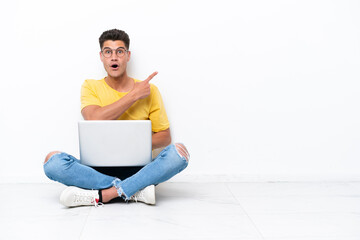 Young man sitting on the floor isolated on white background surprised and pointing side