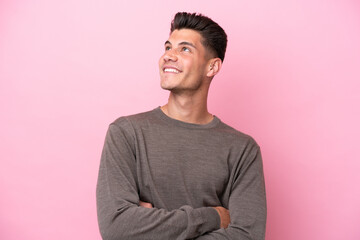 Young caucasian man isolated on pink background looking up while smiling