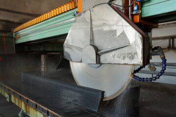 Fast rotating disc with water supply cuts the granite workpiece.
