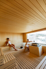 Young couple relaxing in the sauna and watching winter forest through the window