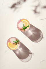 Glasses of fresh pink lemonade layout with ice cubes and rosemary. Summer refreshing cocktails, copy space. Creative spring, summer concept with bright sunny background with harsh shadows, top view.