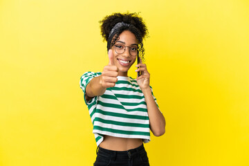 Young african american woman isolated on yellow background keeping a conversation with the mobile while doing thumbs up