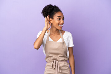 Restaurant waiter latin woman isolated on purple background listening to something by putting hand on the ear