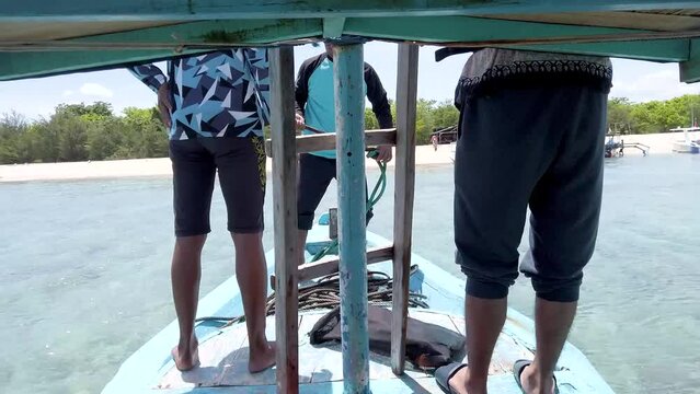 man throwing anker from traditional boat into clear sea with white sand beach