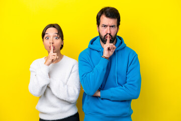 Young caucasian couple isolated on yellow background showing a sign of closing mouth and silence...