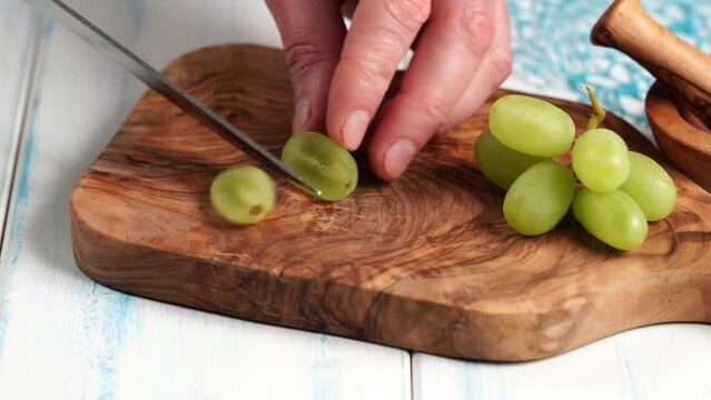 Green grapes without seeds are cut into quarts on a wooden board made of olive wood.