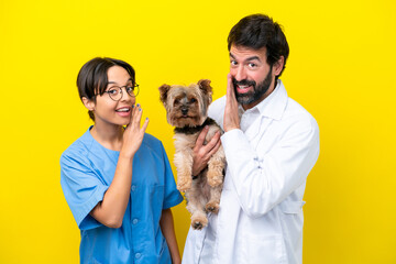 Young veterinarian couple with dog isolated on yellow background whispering something