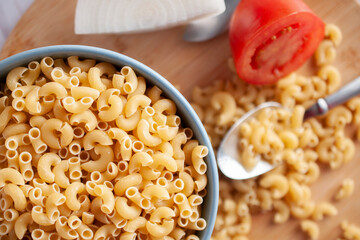 Raw or uncooked Elbow Pasta in a blue bowl and on woodenchooping board.