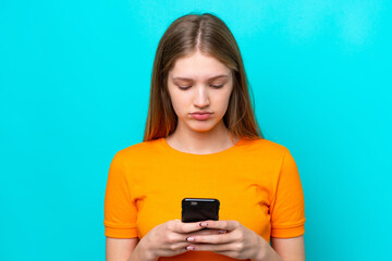 Teenager Russian girl isolated on blue background using mobile phone